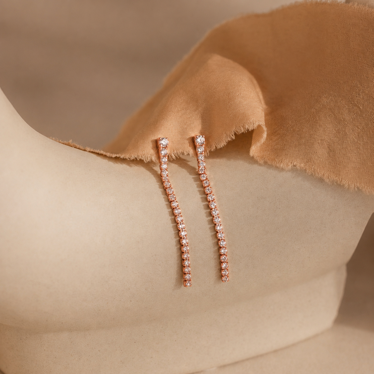 Rose gold earrings with small diamonds on a beige fabric background